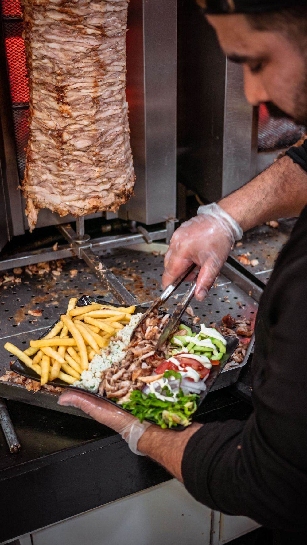 A cook plating grilled meat with fries and fresh salad at a street-food counter