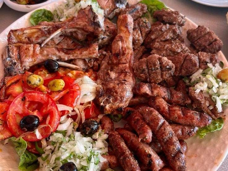Grilled Moroccan meats on a plate: lamb ribs, kefta and sausages with salad and olives