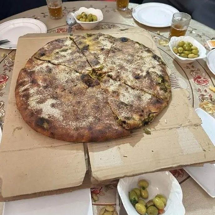A large round Madfouna, the Berber stuffed bread, cut in slices and served with olives and mint tea